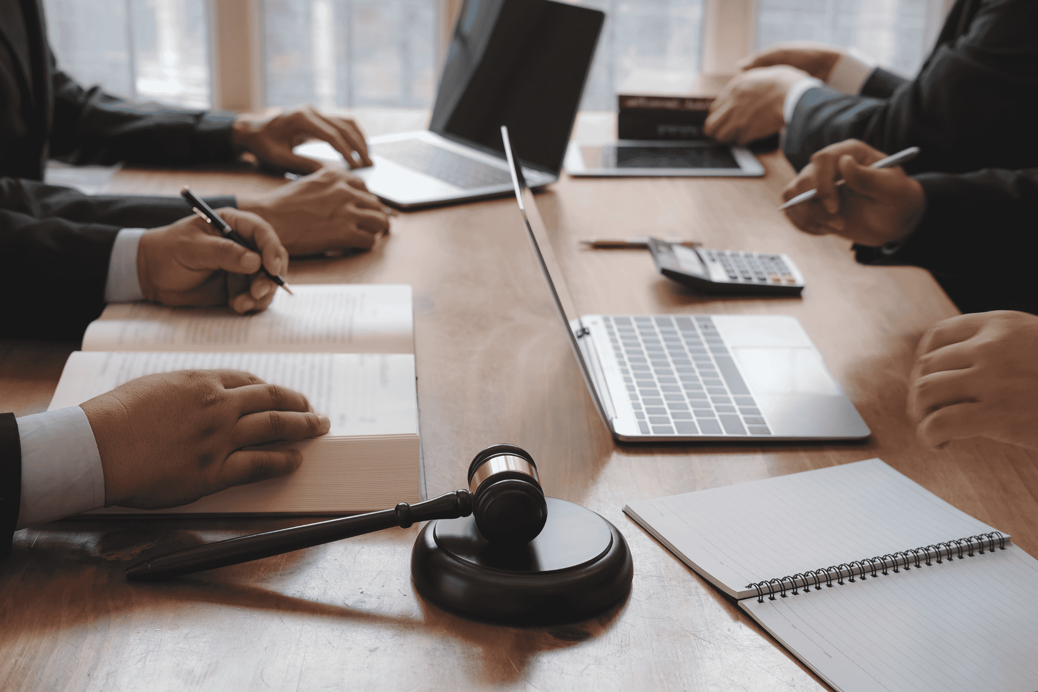 Board meeting in session: diverse professionals discussing documents and laptops around a conference table, with a judge’s gavel in the foreground.