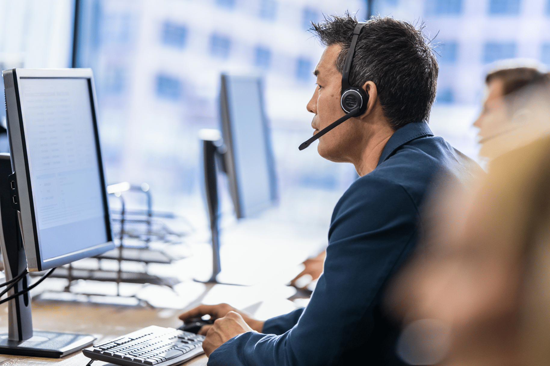 IT support person wearing a headset, speaking at a computer in a bright office