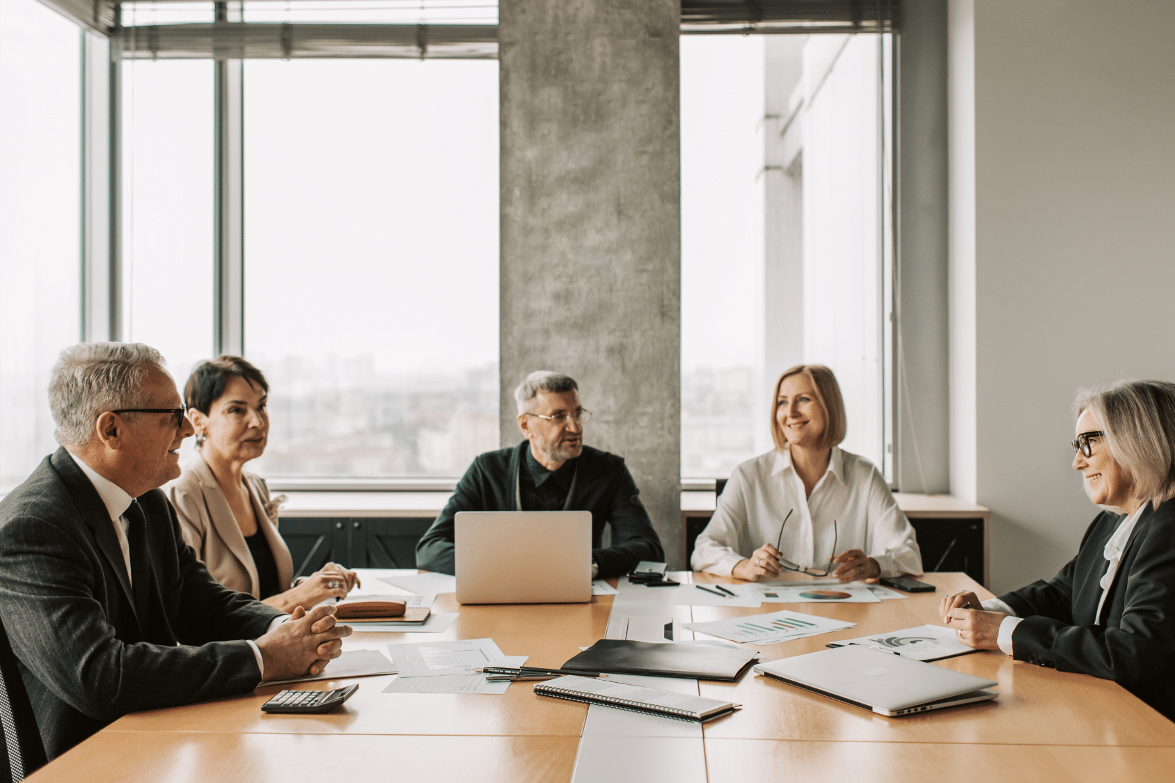 Group of professionals in a meeting around a conference table, talking and smiling