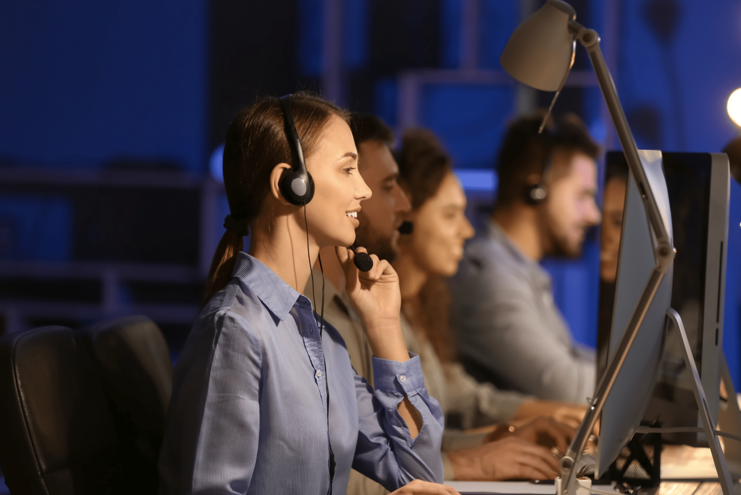 Team members at computers handling IT support requests in a help desk setting.